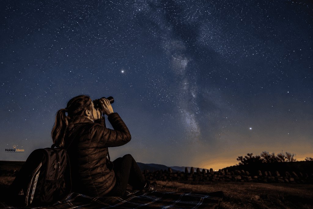 Person using binoculars while stargazing beneath the Milky Way on a clear night, demonstrating how beginners can enjoy stargazing as a hobby without a telescope.