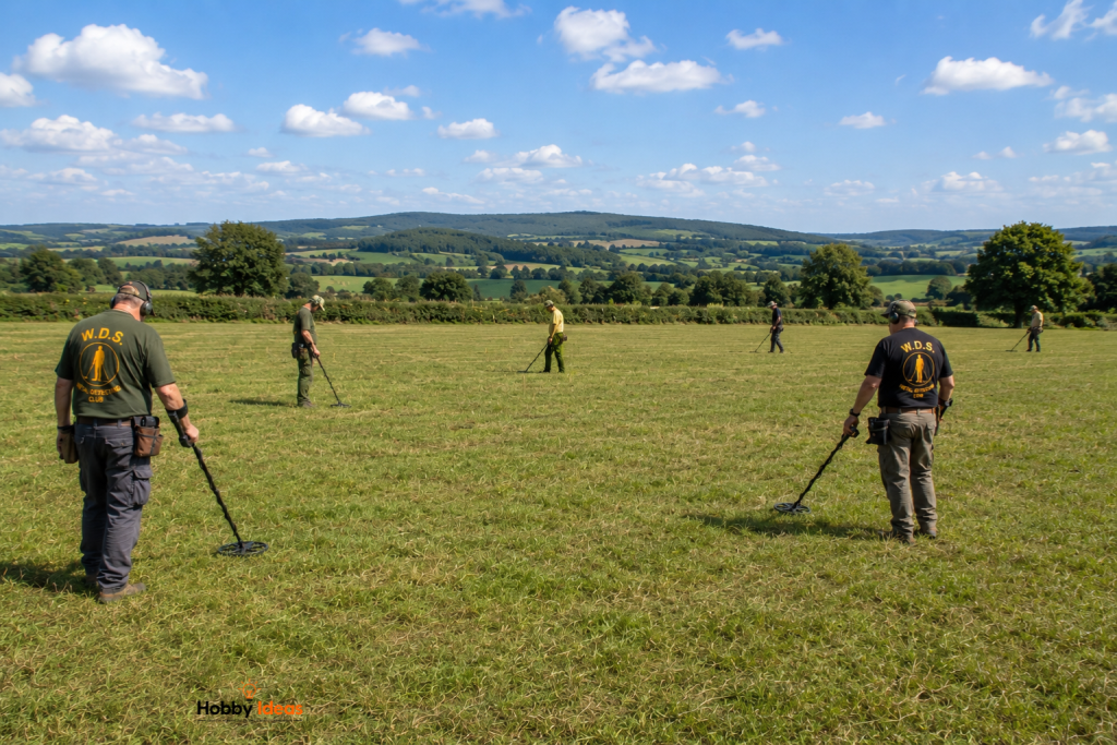 A group of metal detectorists taking part in an organised W.D.C. club dig in the British countryside, searching a grassy field with metal detectors on a sunny day